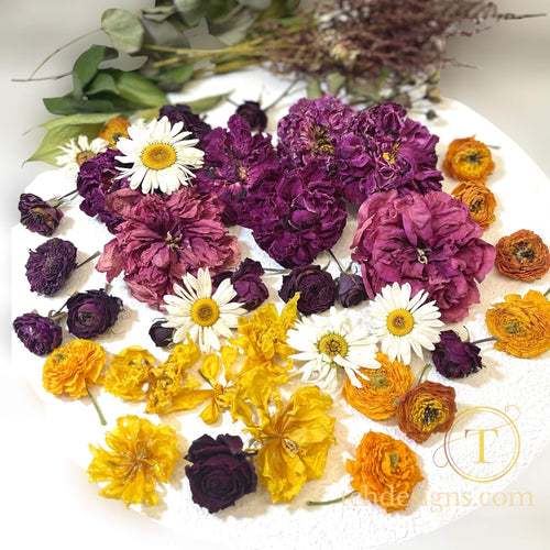Assorted dried flowers including purple, yellow, and white on a white surface with a brand logo in the corner.