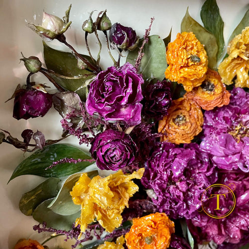 Closeup of epoxy coated roses, orange ranunculus and peonies with green leaves on a white background