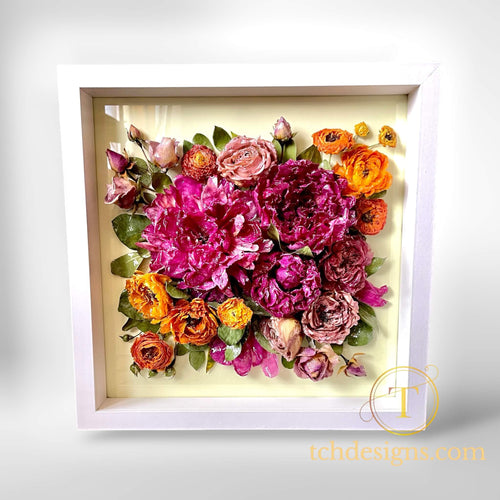 Framed arrangement of pink, orange, and purple flowers with a white border on a light gray background.