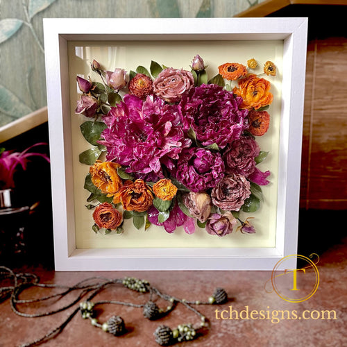 Framed floral arrangement with pink, orange, and purple flowers on a wooden surface.