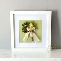 Framed boutonniere with flowers and ribbon on a light gray background
